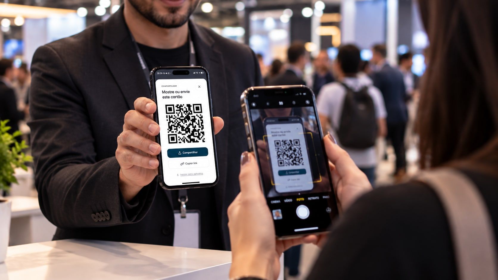 Em uma feira de negócios, visitante aponta a câmera do celular para o QR do cartão digital mostrado por um expositor