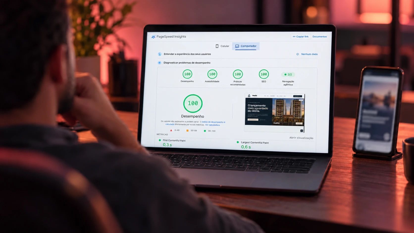 Pessoa olha o notebook com o relatório do PageSpeed Insights: nota 100 em desempenho, acessibilidade, práticas recomendadas e SEO, e o site medido na prévia