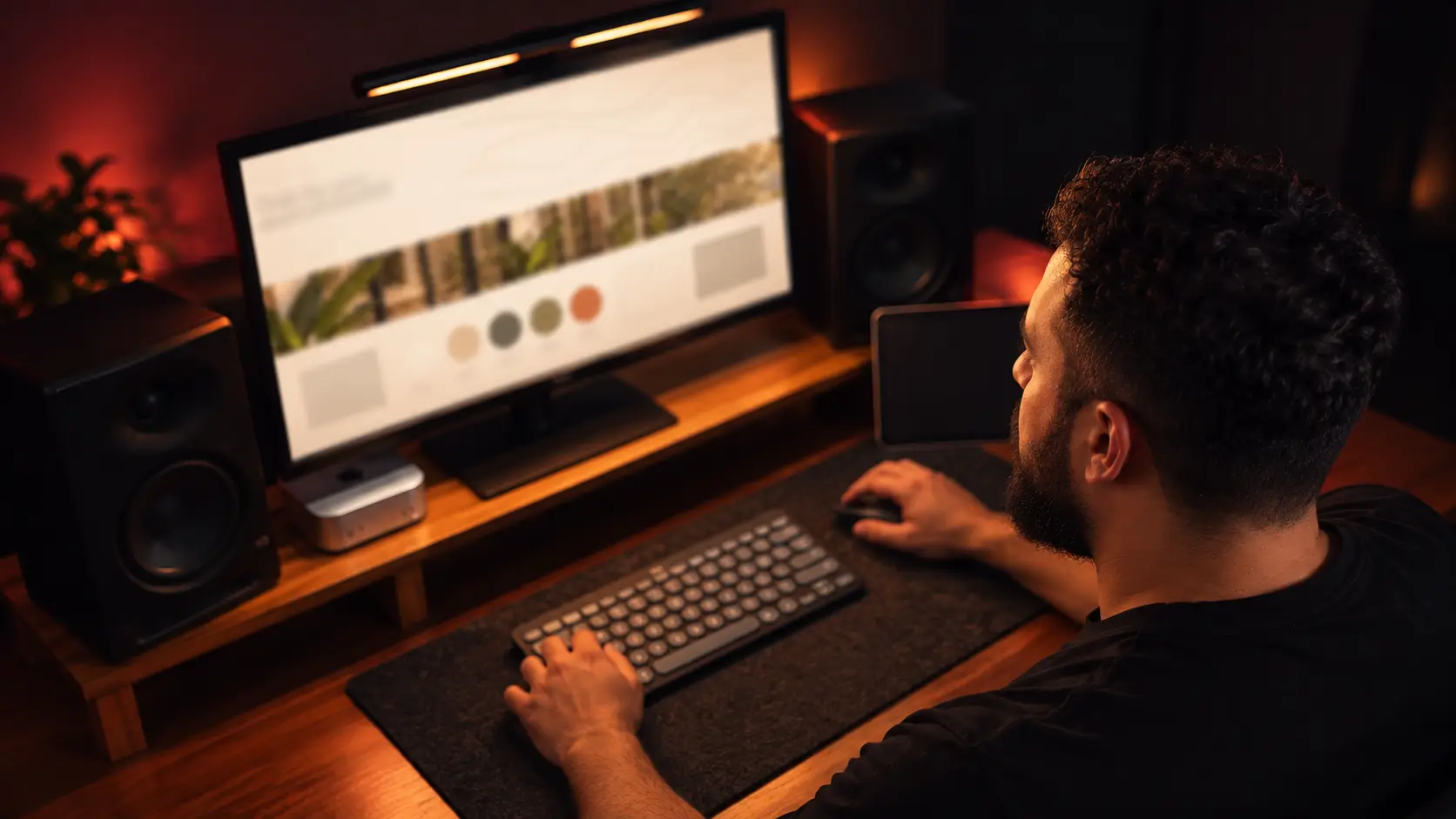 Pessoa diante de um monitor com a paleta de cores de uma marca aberta, numa mesa de madeira iluminada por luz quente.